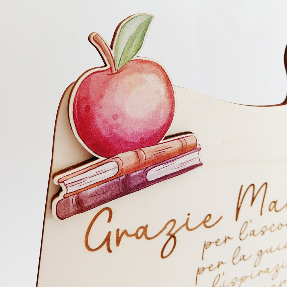 Dettaglio mela e libri sulla targa puzzle in legno dedicata alla maestra