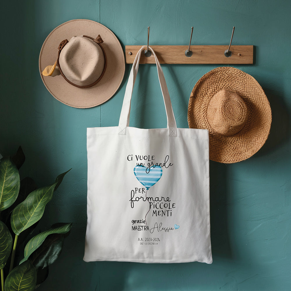 Tote bag maestra personalizzata con frase piccole menti e cuore azzurro, shopper in cotone su parete azzurra