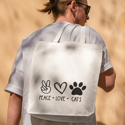 Una persona con occhiali da sole e camicia bianca porta con sé la borsa Tote con illustrazioni de Il mio negozio, con icone nere della pace, del cuore e della zampa con la scritta "Peace Love Cats" - un regalo originale e personalizzato per gli amanti dei gatti.